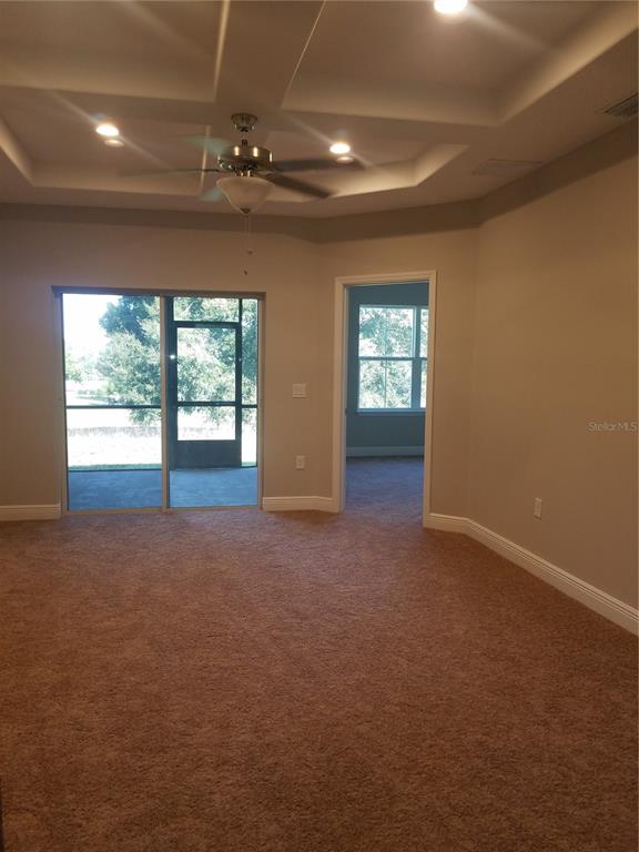 A carpeted room features a tray ceiling with a fan and a sliding glass door — 8504 MAGNIFICENT LANE, GROVELAND, FL
