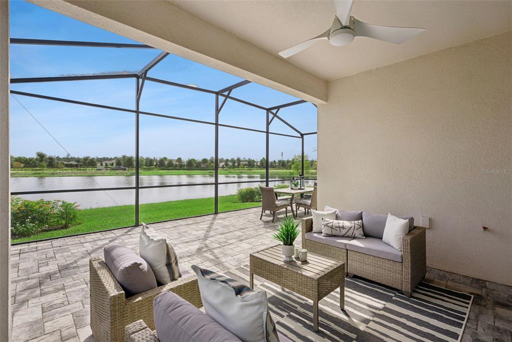 A covered patio features wicker furniture, a ceiling fan, and a screened enclosure overlooking a lake — 2499 CLIFF WAY, ST CLOUD, FL