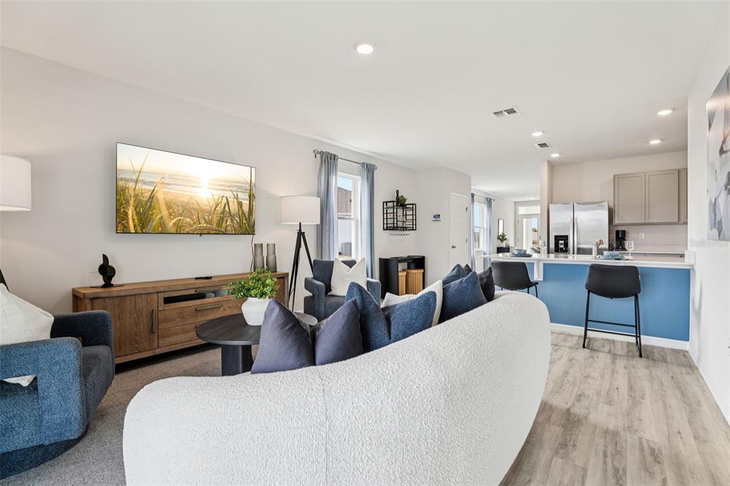 A living room with a curved sofa, blue accent chairs, and an open-concept kitchen — 4129 GIORGIO DRIVE, WINTER HAVEN, FL