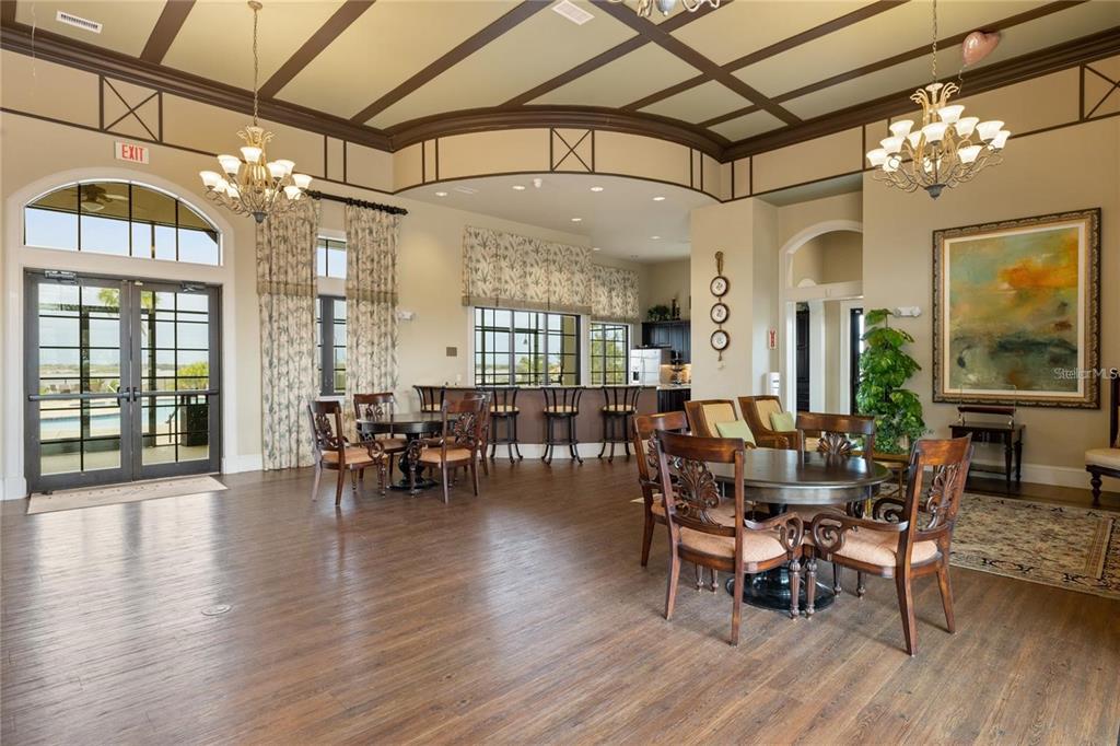 A spacious clubhouse room features wood flooring, two chandeliers, dining tables, and a bar area — 402 WATERFERN TRAIL DRIVE, AUBURNDALE, FL