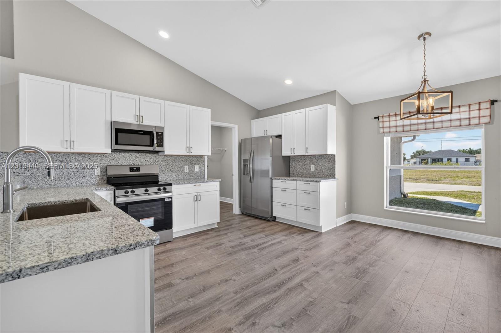 A kitchen features white cabinets, granite countertops, stainless steel appliances, and wood-look flooring — 409 NE 25th Ter, Cape Coral FL 33909, CAPE CORAL, FL