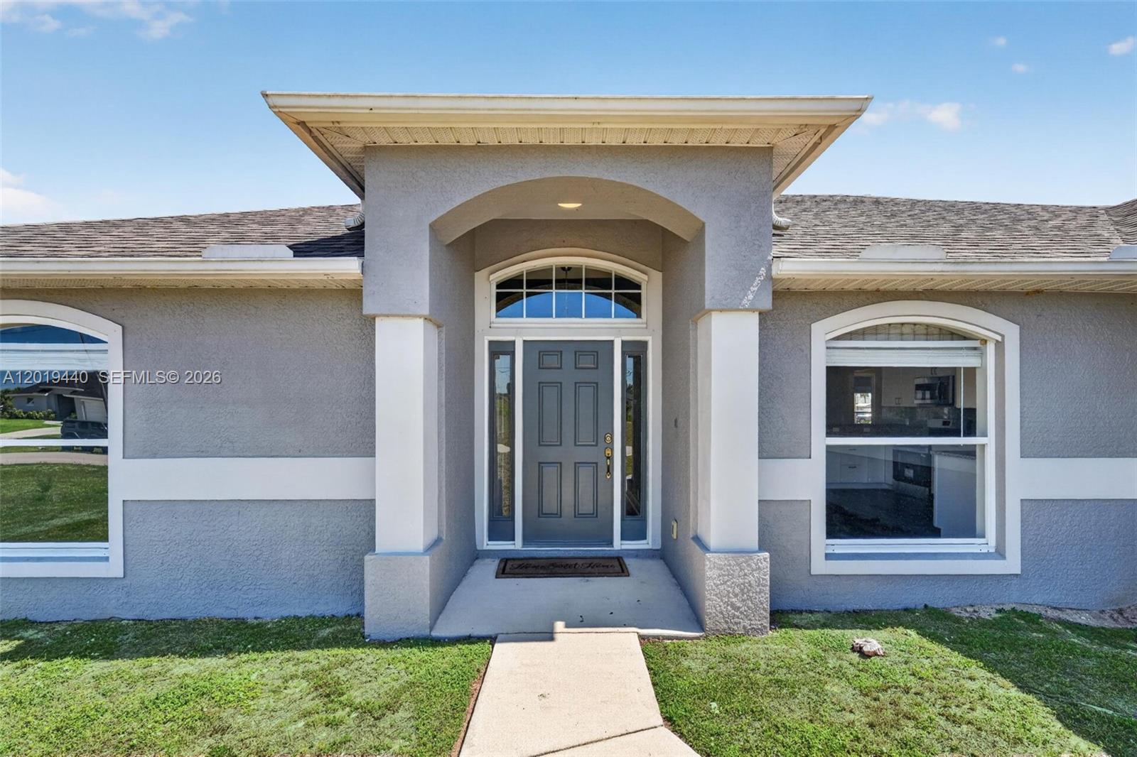 A single-story gray stucco house features a two-car garage and a concrete walkway — 409 NE 25th Ter, Cape Coral FL 33909, CAPE CORAL, FL