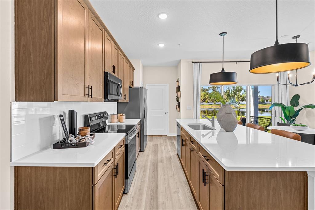 A modern kitchen features wood cabinets, white countertops, stainless steel appliances, and a central island — 4947 WINDING RIVER ROAD, ORLANDO, FL
