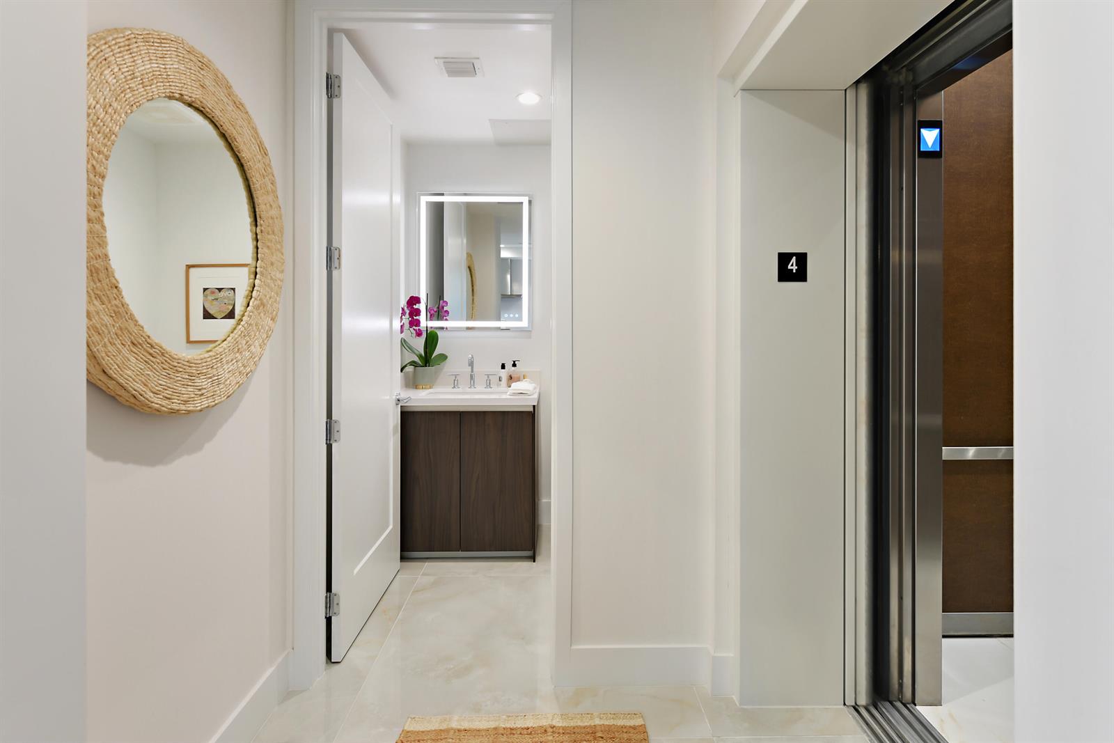 A hallway features a round woven mirror, an open door to a bathroom, and an elevator — 485 E Royal Palm Road # 403, Boca Raton FL 33432, BOCA RATON, FL