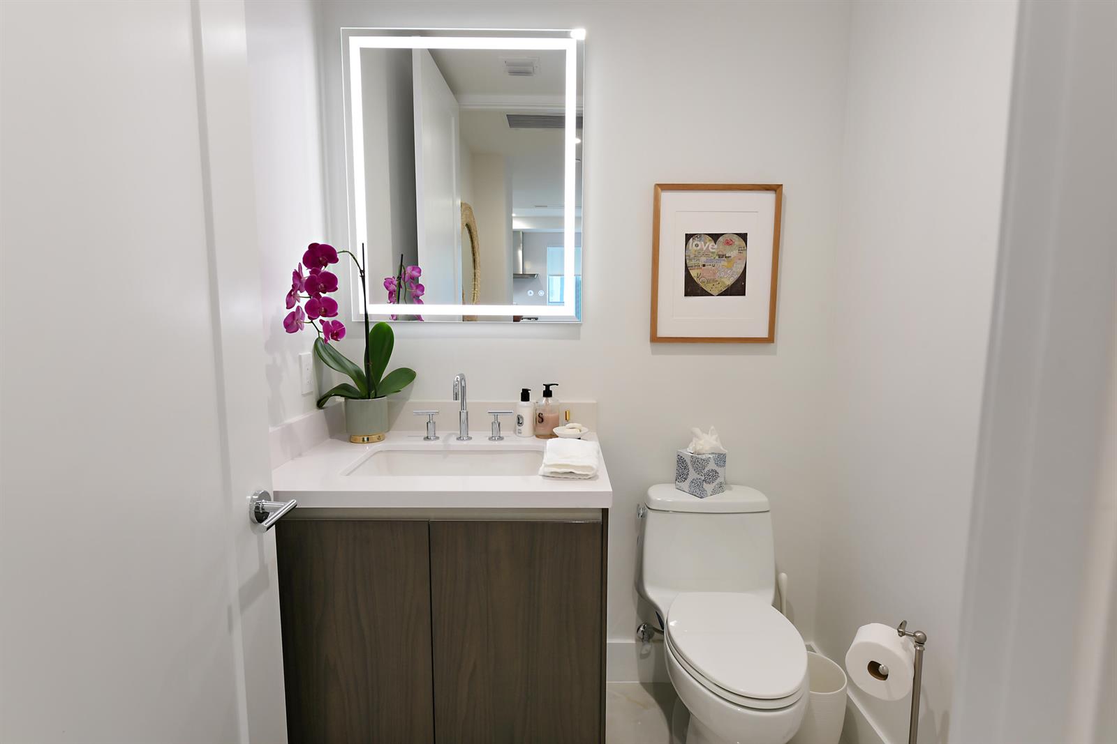 A modern powder room features a dark wood vanity, white countertop, and a backlit mirror — 485 E Royal Palm Road # 403, Boca Raton FL 33432, BOCA RATON, FL