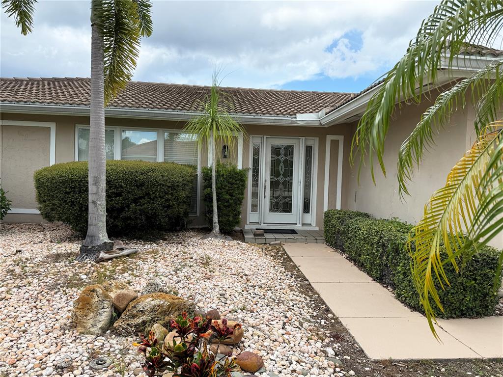 The exterior of a single-story house features a tiled roof, a white front door, and landscaping — 821 VIA TUNIS, PUNTA GORDA, FL