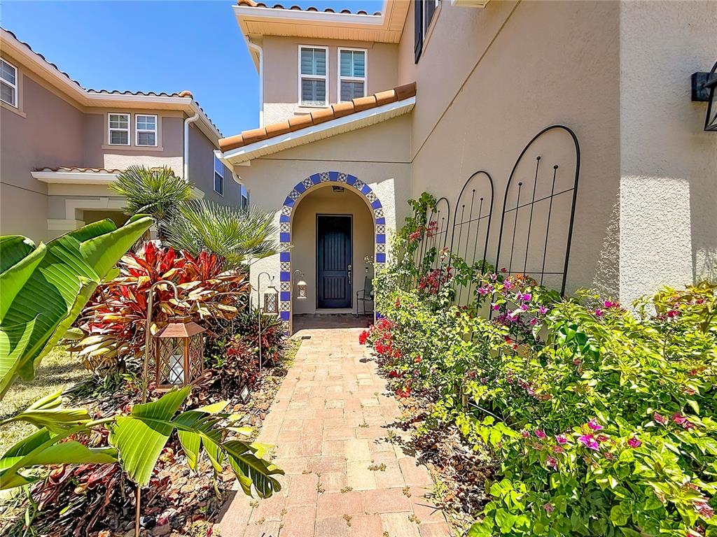 A paved walkway leads to a front entrance featuring a blue tiled arched doorway — 10193 GRAND OAK CIRCLE, MADEIRA BEACH, FL