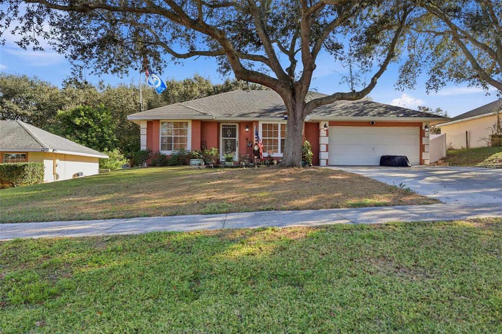 A single-story house with a white garage door, red stucco exterior, and a large tree — 4254 WORTHINGTON PLACE, MASCOTTE, FL