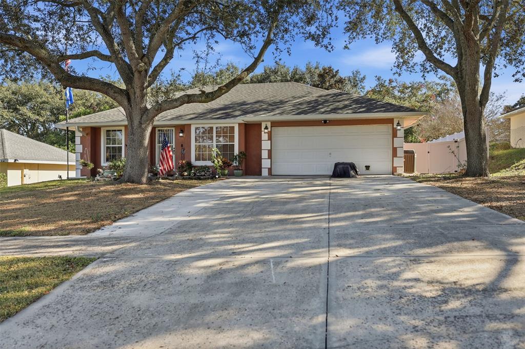 A single-story house with a two-car garage, terracotta-colored walls, and large oak trees — 4254 WORTHINGTON PLACE, MASCOTTE, FL