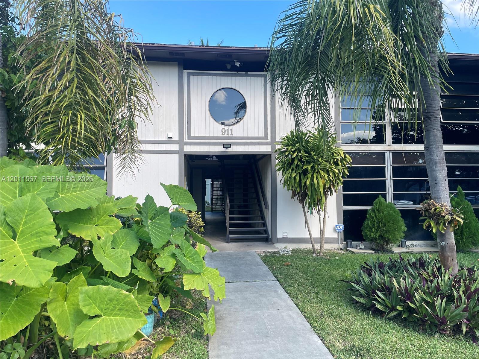 A two-story apartment building exterior features a circular window, a central staircase, and landscaping — 911 NE 199th St # 14, Miami FL 33179, MIAMI, FL