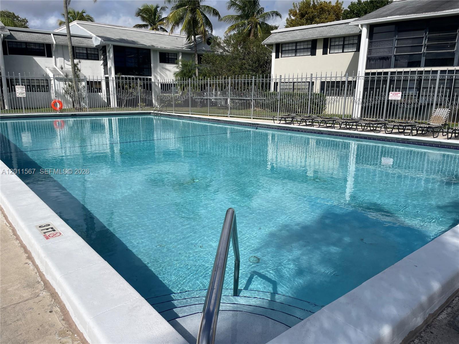 A rectangular swimming pool with a metal handrail sits in front of two-story apartment buildings — 911 NE 199th St # 14, Miami FL 33179, MIAMI, FL