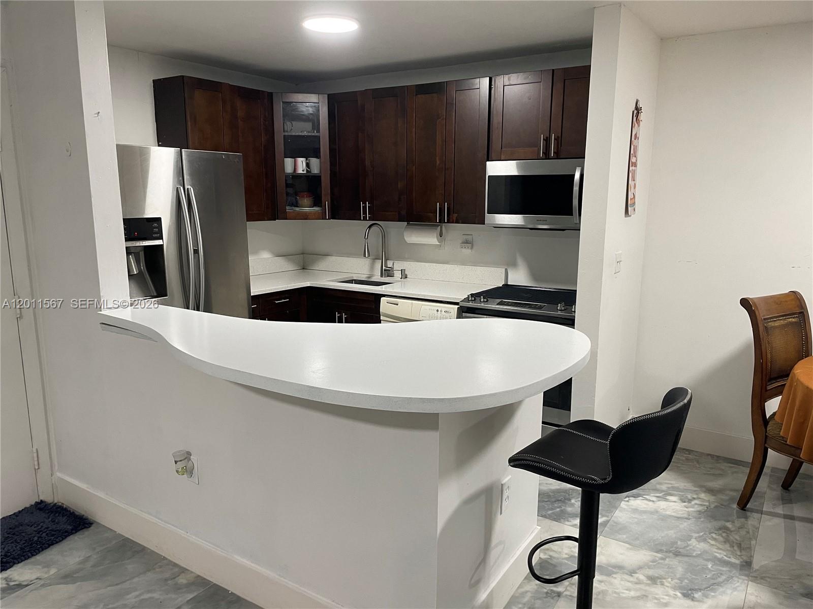 A kitchen features dark wood cabinets, stainless steel appliances, and a white curved breakfast bar — 911 NE 199th St # 14, Miami FL 33179, MIAMI, FL