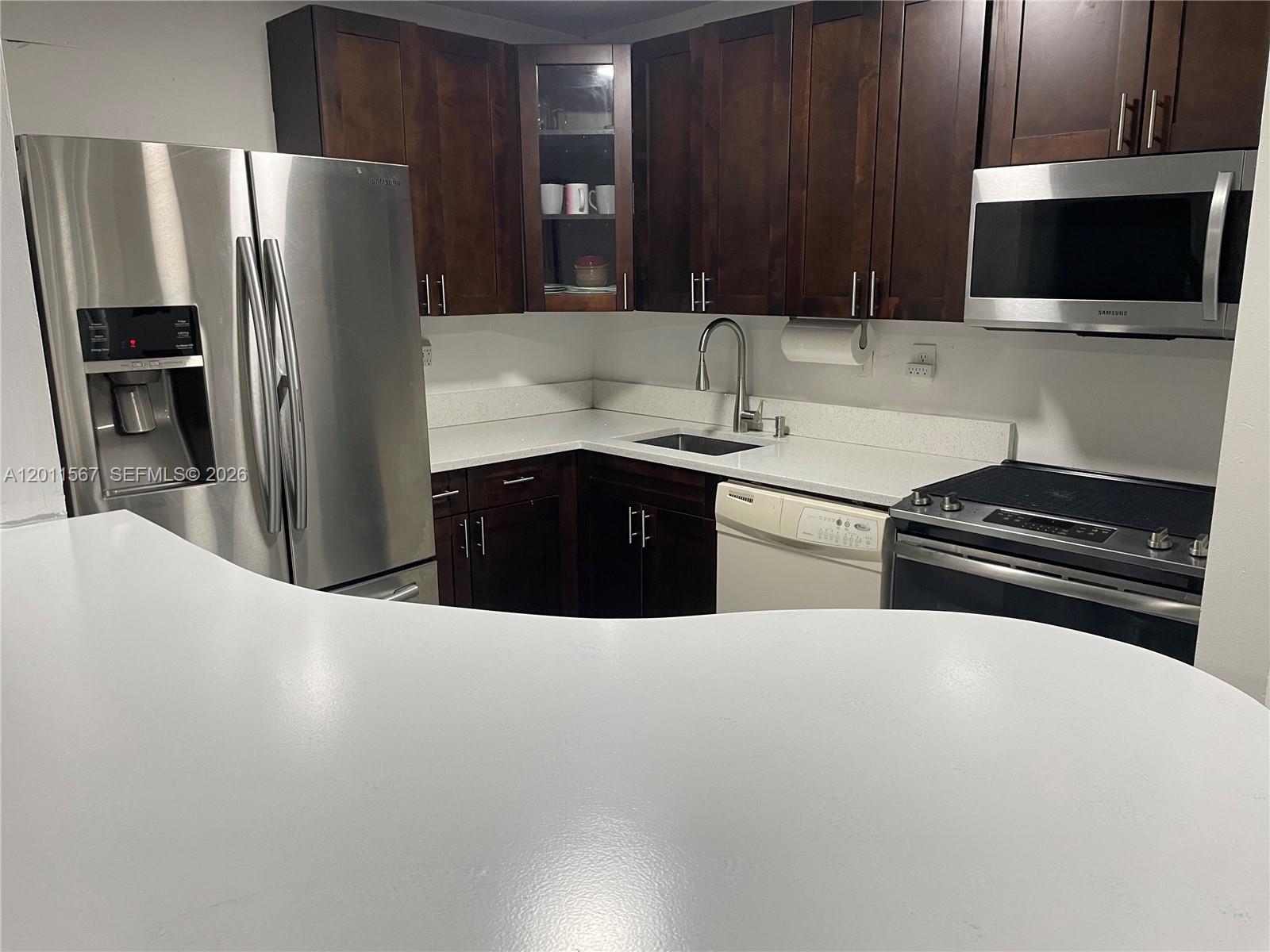A kitchen features dark wood cabinets, stainless steel appliances, and white countertops — 911 NE 199th St # 14, Miami FL 33179, MIAMI, FL