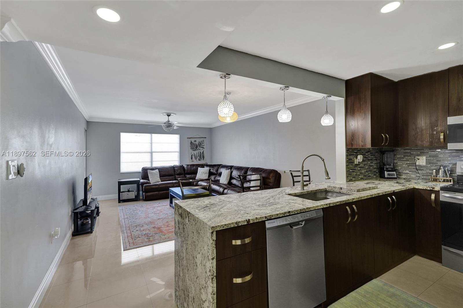 An open-concept kitchen with granite countertops overlooks a living room with a brown sectional sofa — 4314 NW 9th Ave # 3D, Deerfield Beach FL 33064, DEERFIELD BEACH, FL