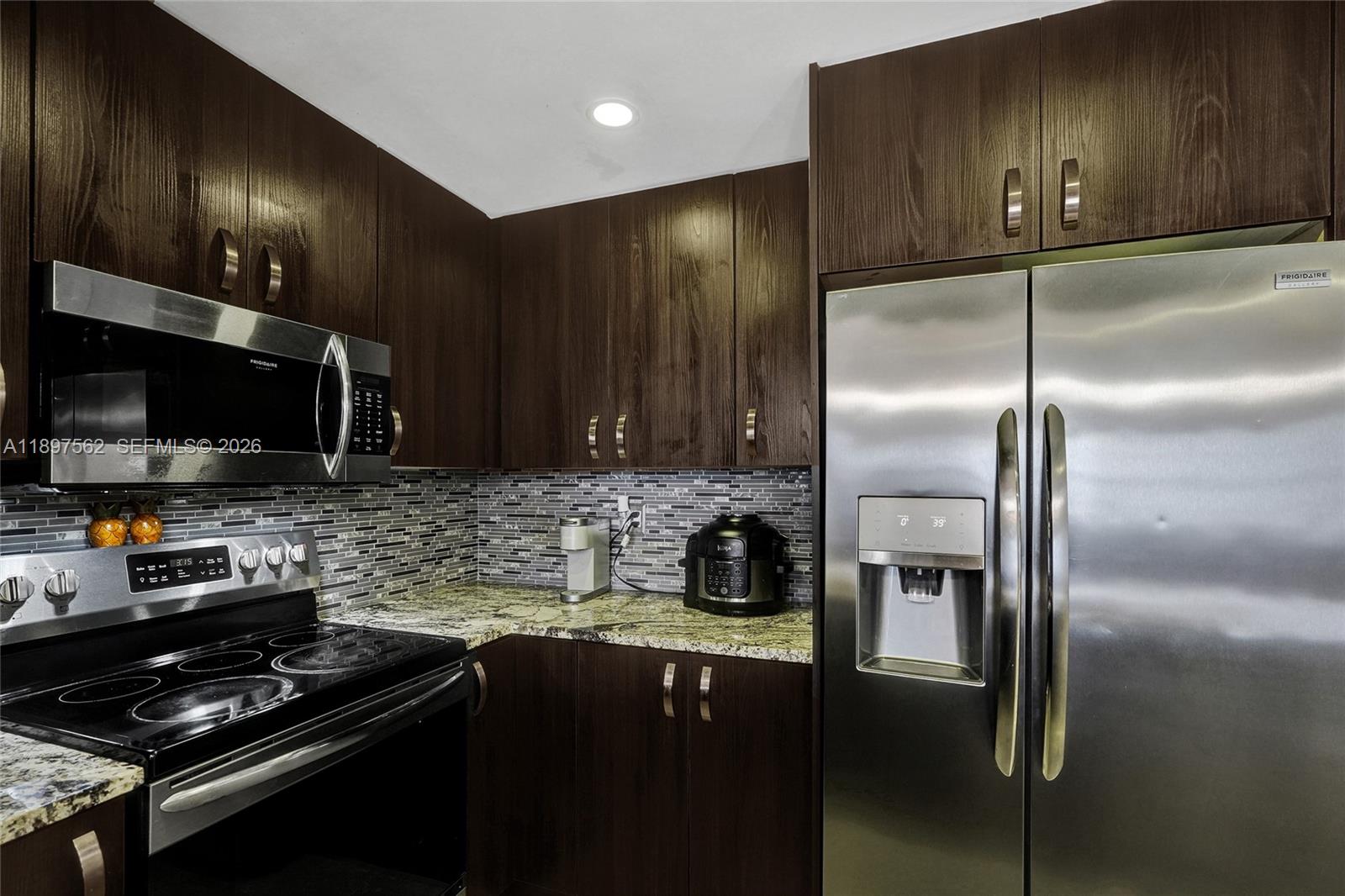 A kitchen features dark wood cabinets, stainless steel appliances, and a mosaic tile backsplash — 4314 NW 9th Ave # 3D, Deerfield Beach FL 33064, DEERFIELD BEACH, FL