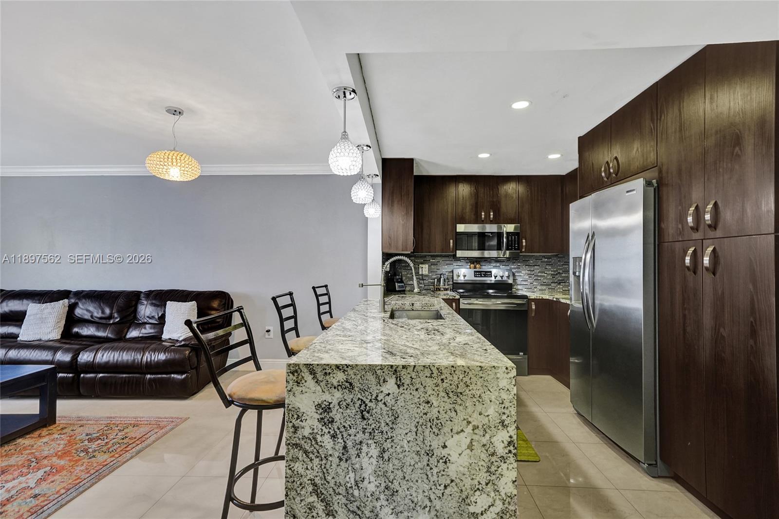 A kitchen features dark wood cabinets, granite countertops, stainless steel appliances, and a breakfast bar — 4314 NW 9th Ave # 3D, Deerfield Beach FL 33064, DEERFIELD BEACH, FL
