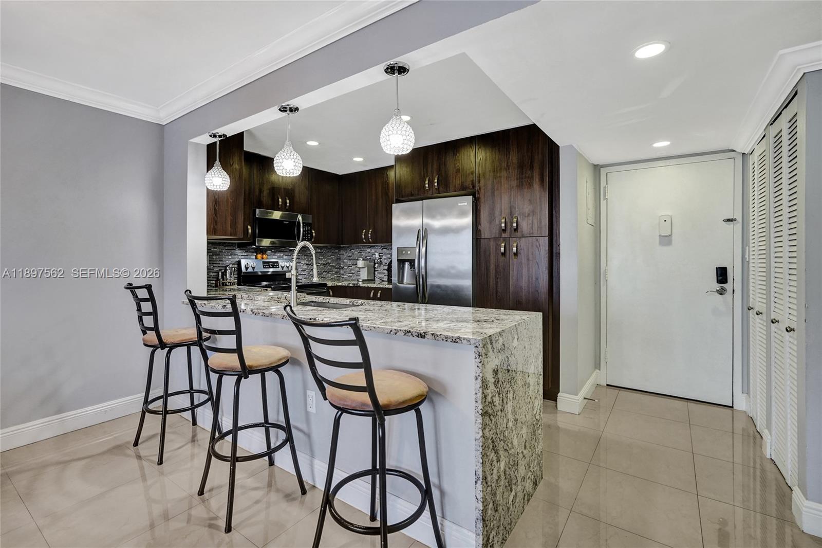 A kitchen features dark wood cabinets, granite countertops, a breakfast bar, and three metal stools — 4314 NW 9th Ave # 3D, Deerfield Beach FL 33064, DEERFIELD BEACH, FL