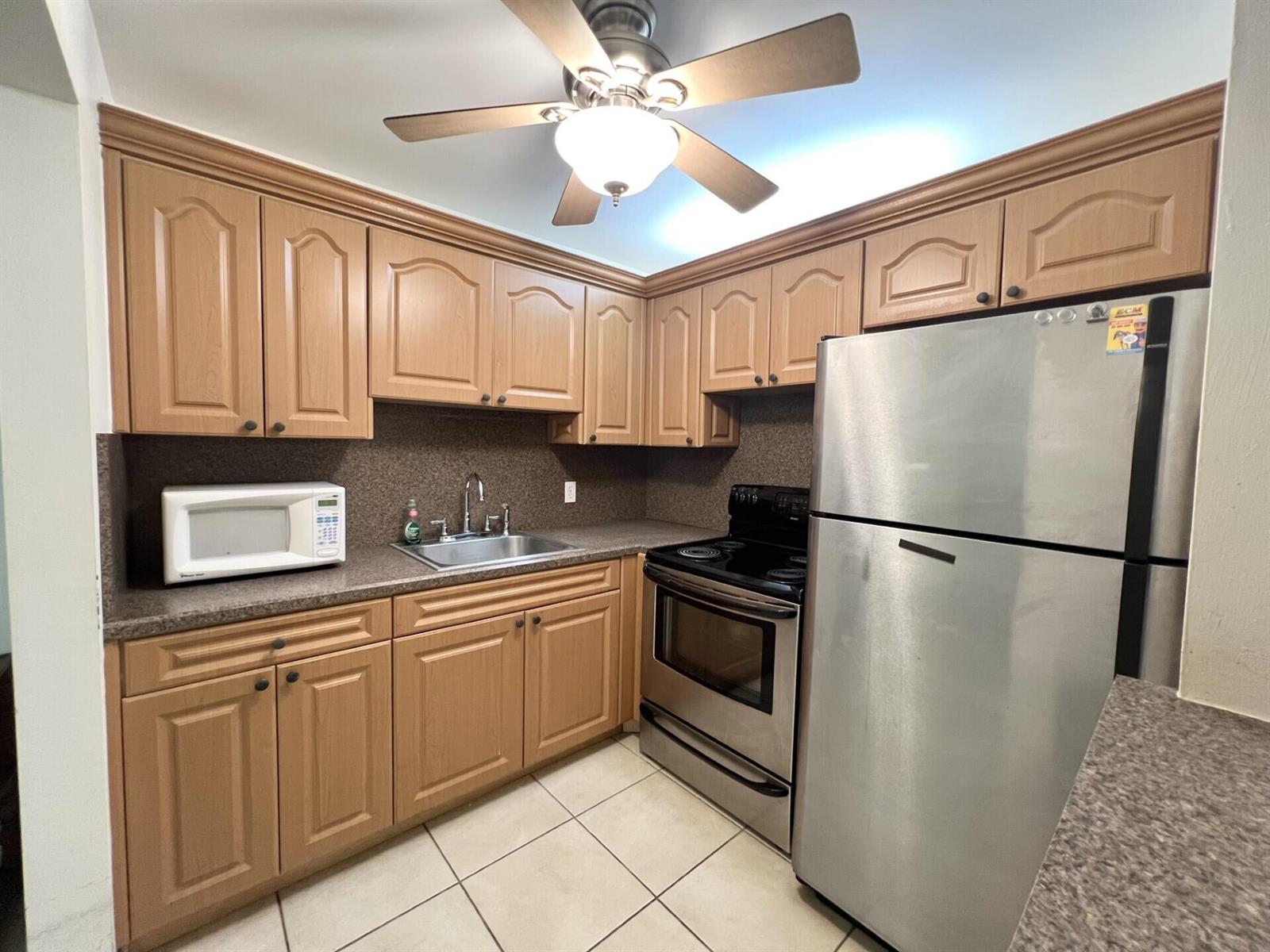 A kitchen features wood cabinets, stainless steel appliances, a sink, and a ceiling fan — 4023 Berkshire B # 4023, Deerfield Beach FL 33442, DEERFIELD BEACH, FL