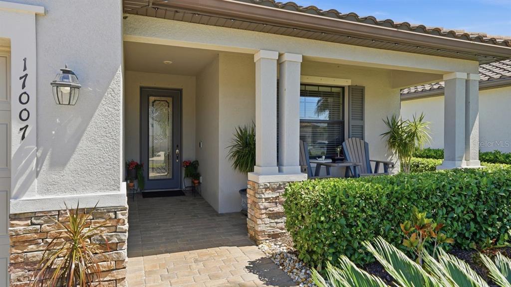 The front entrance of a house features a stone-accented porch, a glass door, and landscaping — 17007 BLUE RIDGE PLACE, BRADENTON, FL