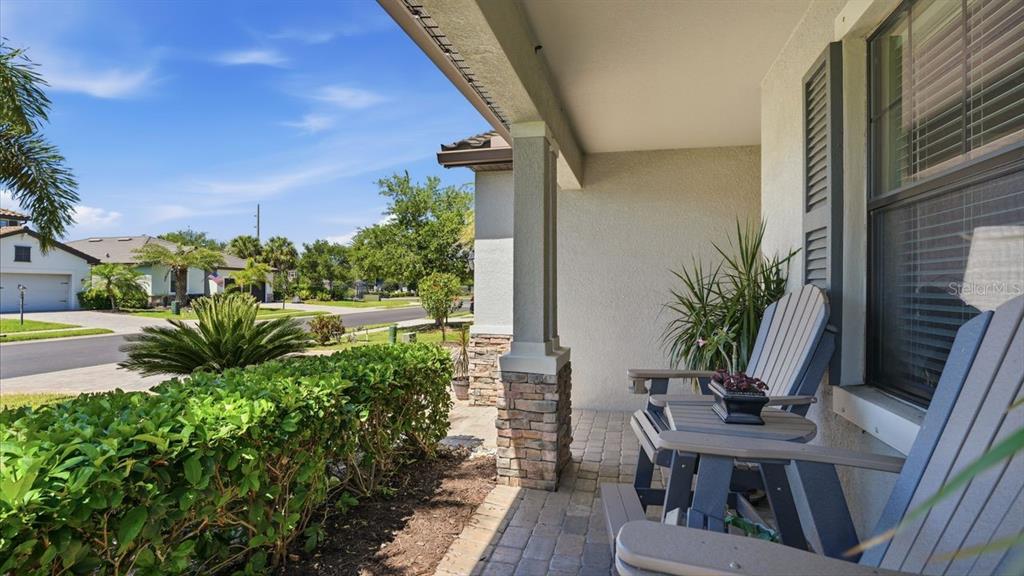 A covered front porch features stone-based columns, paver flooring, and two Adirondack chairs — 17007 BLUE RIDGE PLACE, BRADENTON, FL