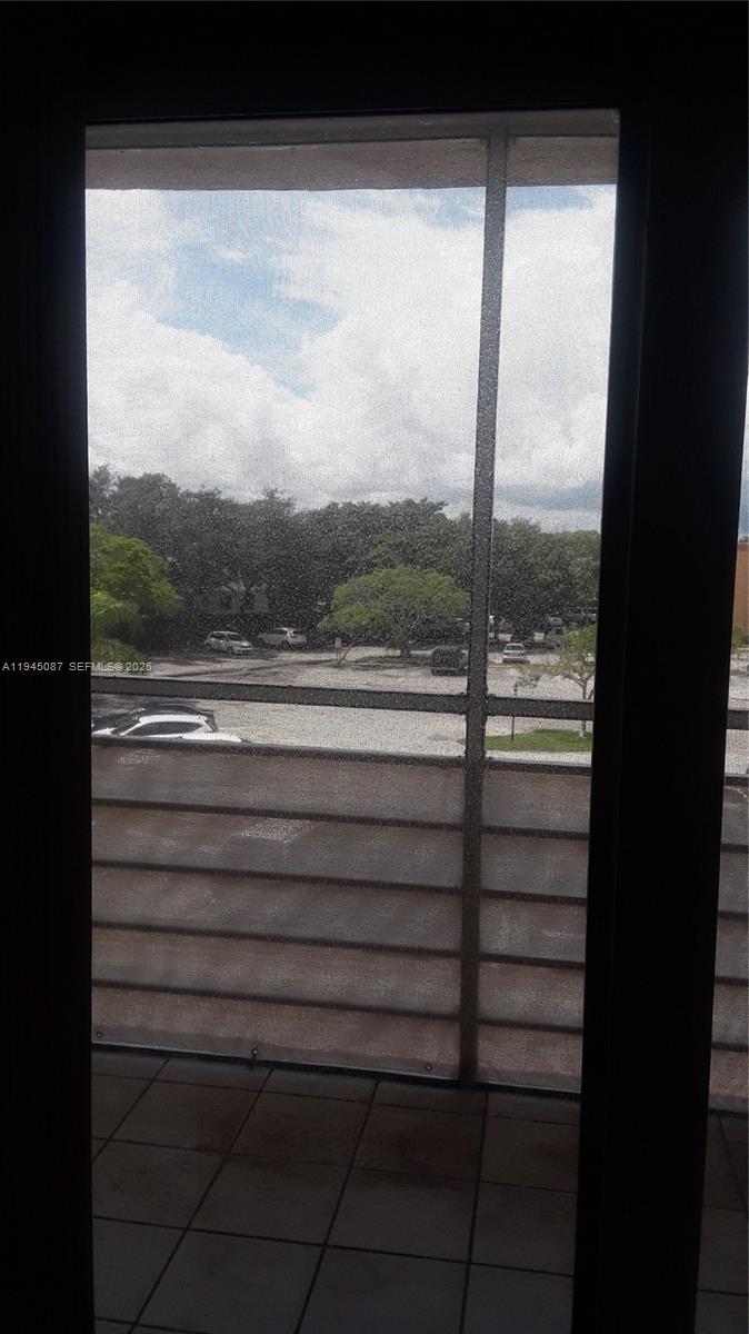 A view of a parking lot and trees seen through a screened-in balcony door — 4374 NW 9th Ave # 3G, Deerfield Beach FL 33064, DEERFIELD BEACH, FL