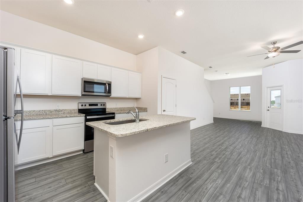 A kitchen with white cabinets, granite countertops, and stainless steel appliances opens to a living area — 648 POPPY LANE, DUNDEE, FL