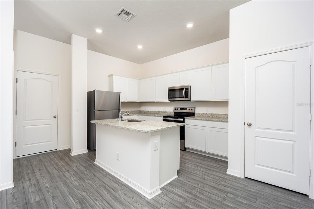 A kitchen with white cabinets, granite countertops, stainless steel appliances, and gray wood-look flooring — 648 POPPY LANE, DUNDEE, FL