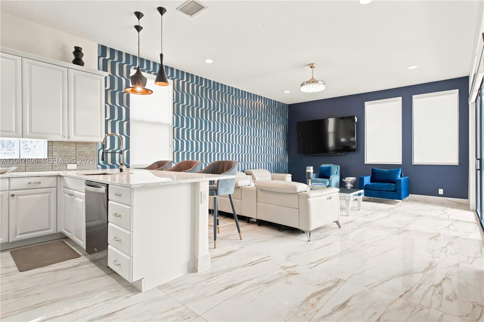 A modern open-concept kitchen and living area features patterned wallpaper, white cabinetry, and marble flooring — 3061 SW 189th Ter, Miramar FL 33029, MIRAMAR, FL