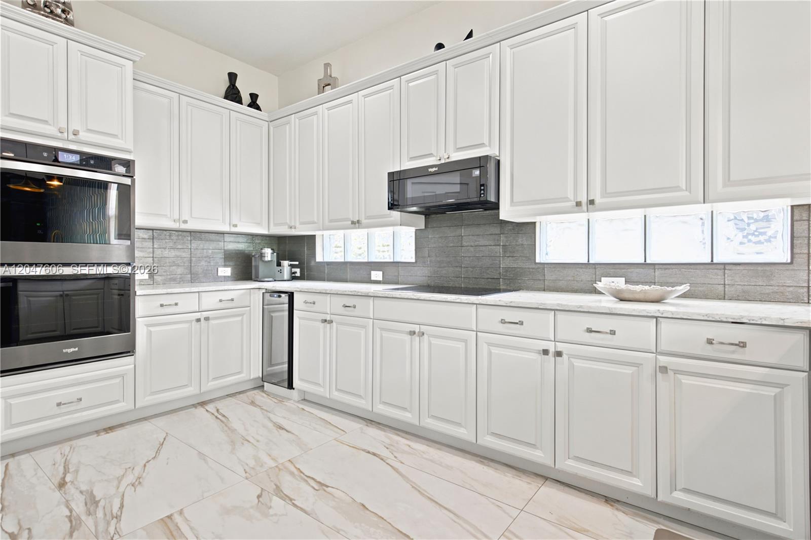 A kitchen features white cabinets, a black oven and microwave, and marble-patterned tile flooring — 3061 SW 189th Ter, Miramar FL 33029, MIRAMAR, FL