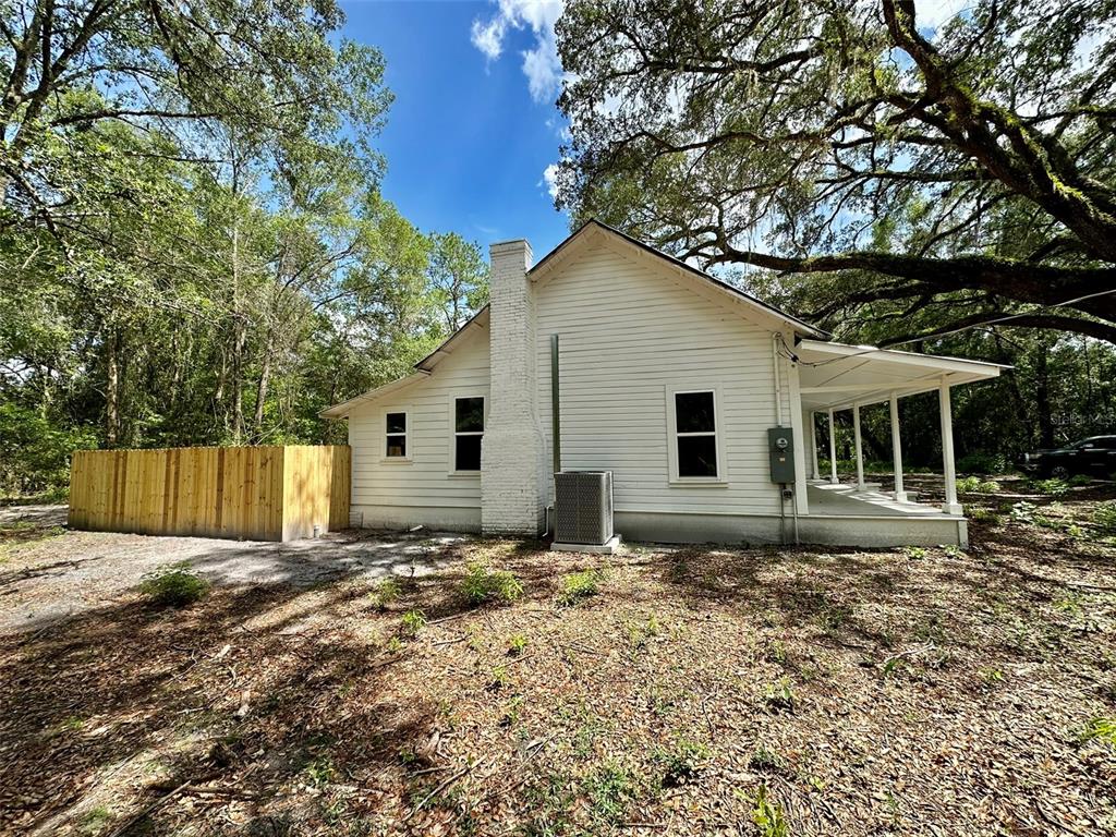 A white house with a brick chimney, a side porch, and a wooden privacy fence — 13647 NE 141ST DRIVE, WALDO, FL