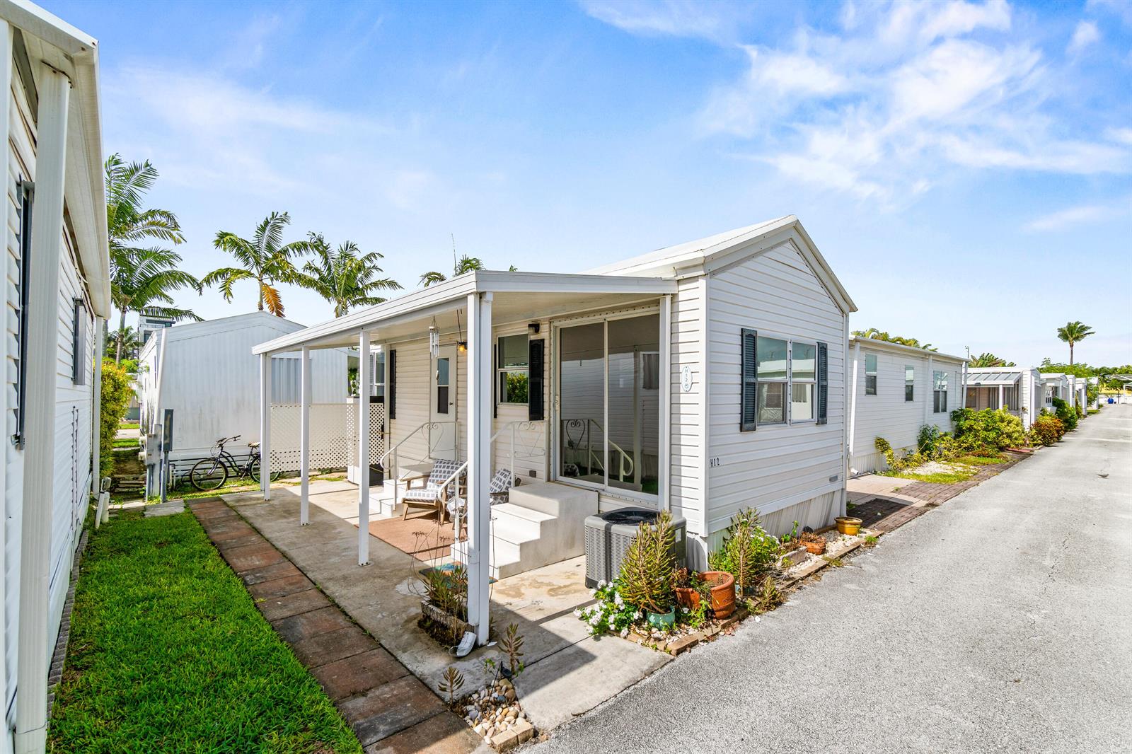 A white mobile home features a covered patio, sliding glass doors, and a paved driveway — 12 Hibiscus Drive # H, Briny Breezes FL 33435, BRINY BREEZES, FL