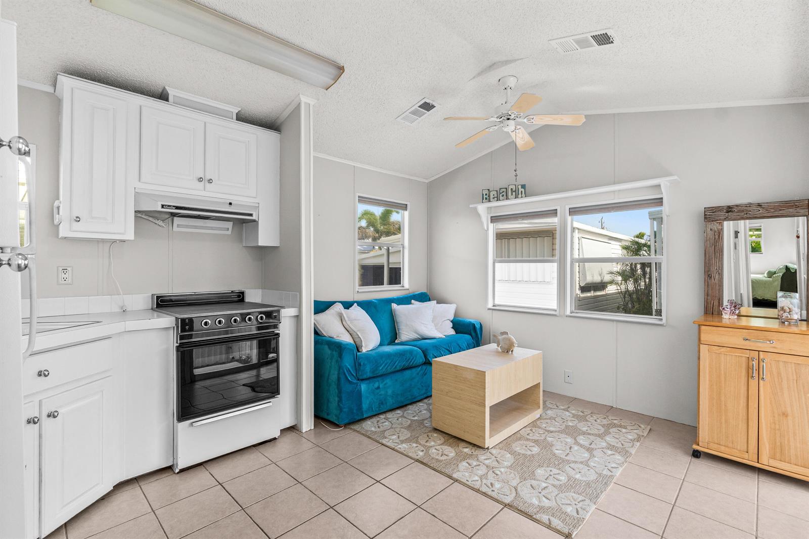 A small kitchen and living area with a blue sofa, light wood table, and tile floors — 12 Hibiscus Drive # H, Briny Breezes FL 33435, BRINY BREEZES, FL