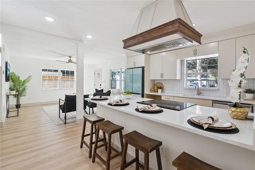 A modern open-concept kitchen features a white quartz island, wooden stools, and a range hood — 1931 CLOVERLAWN AVENUE, ORLANDO, FL