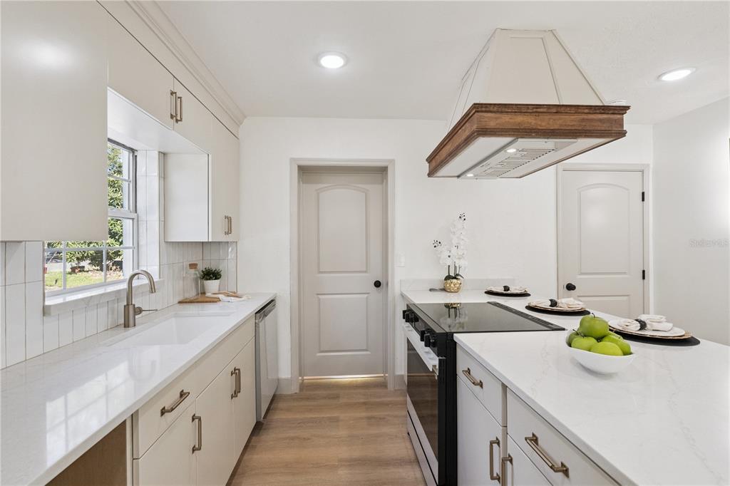 A modern kitchen features white cabinets, quartz countertops, a wooden range hood, and stainless appliances — 1931 CLOVERLAWN AVENUE, ORLANDO, FL