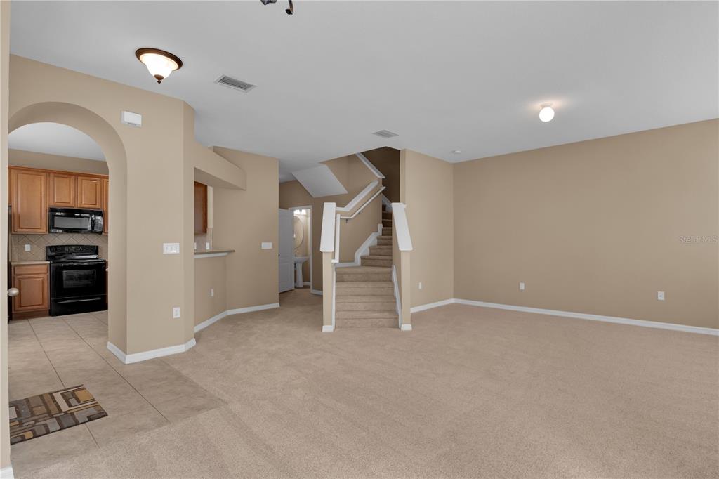 An open living area features beige carpeting, a staircase, and an adjacent kitchen with cabinets — 7001 INTERBAY BOULEVARD UNIT 119, TAMPA, FL