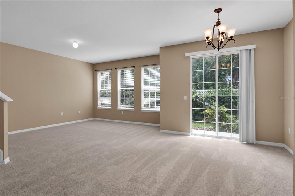 An empty living room features beige walls, carpeted flooring, three windows, and a sliding glass door — 7001 INTERBAY BOULEVARD UNIT 119, TAMPA, FL