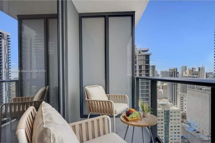 A balcony with modern chairs and a small table overlooking a city skyline — 159 NE 6th St # 3004, Miami FL 33132, MIAMI, FL