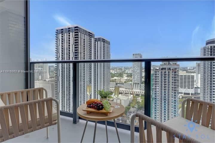 A balcony with two chairs and a small table overlooking a city skyline — 159 NE 6th St # 3004, Miami FL 33132, MIAMI, FL