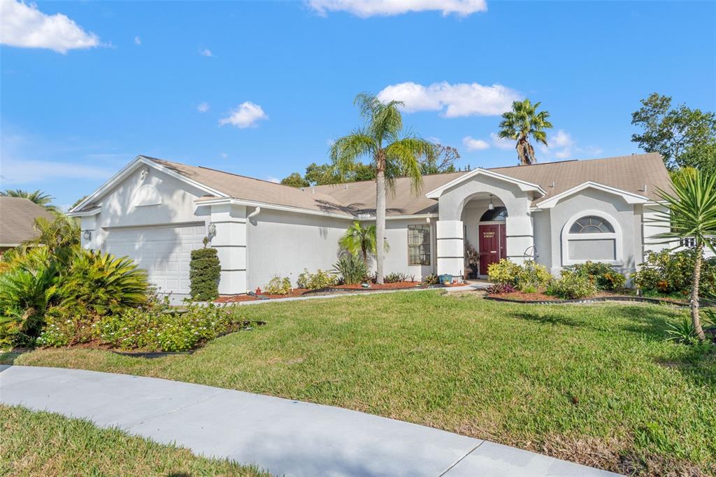 A single-story house with a white stucco exterior, a red front door, and a lawn — 13732 TRIUMPH COURT, HUDSON, FL