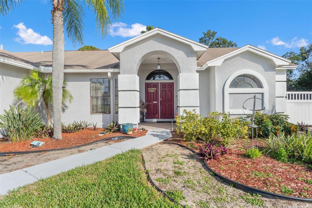 A single-story house with a white stucco exterior, red double front doors, and a palm tree — 13732 TRIUMPH COURT, HUDSON, FL