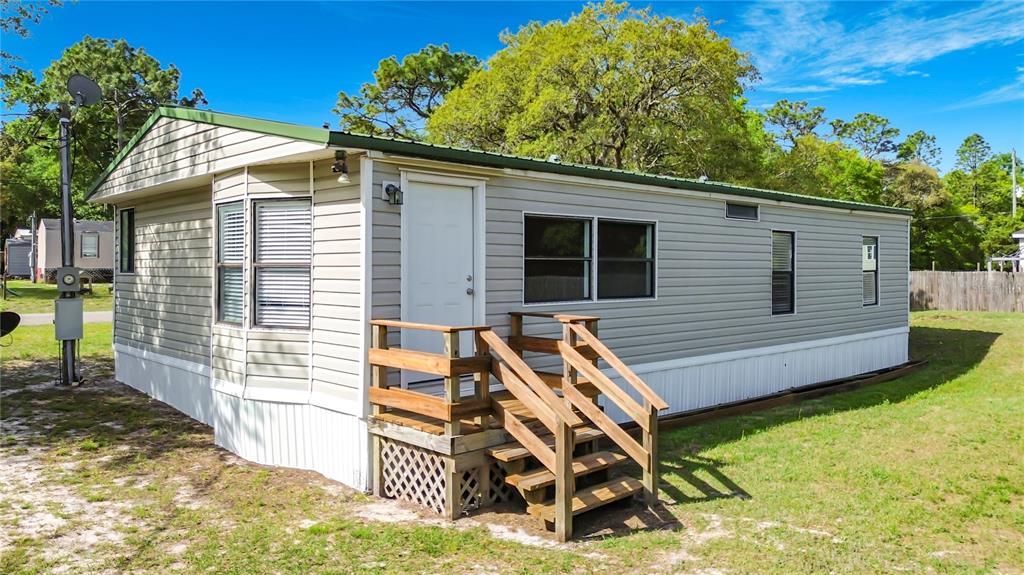 A single-story mobile home with light gray siding and a wooden staircase leading to the entrance — 7429 W REVERE LANE, HOMOSASSA, FL