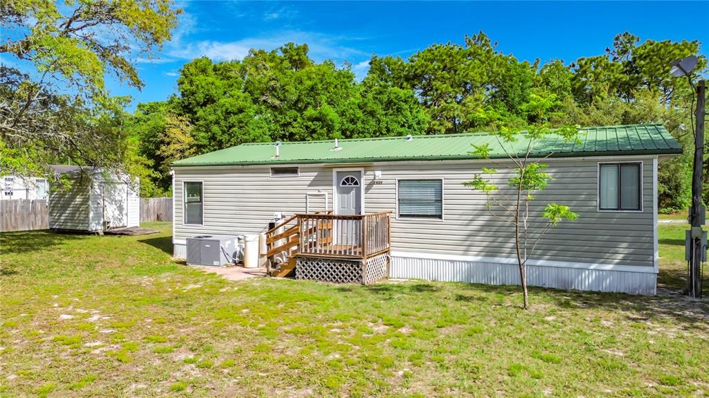 A light-colored mobile home with a green metal roof sits on a grassy lot — 7429 W REVERE LANE, HOMOSASSA, FL