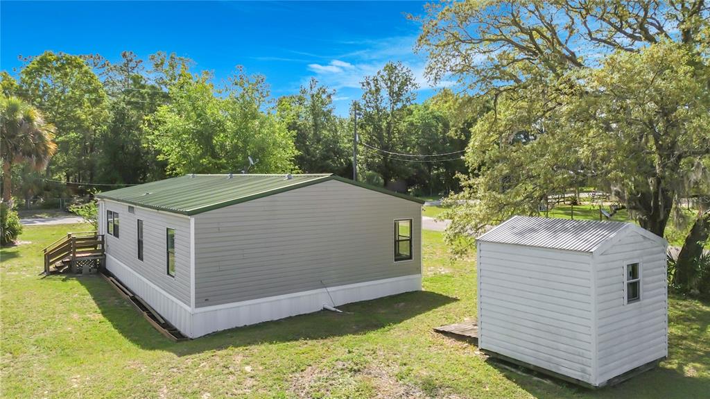 A gray mobile home with a green metal roof sits next to a small shed — 7429 W REVERE LANE, HOMOSASSA, FL