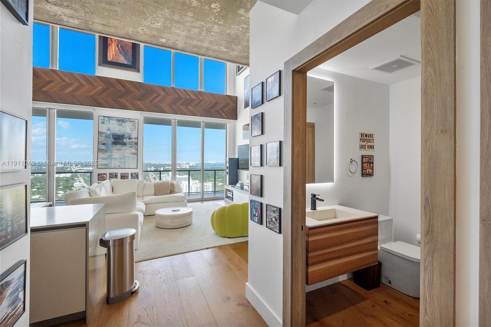 A modern living room with floor-to-ceiling windows and an adjacent bathroom with a wood vanity — 3470 E Coast Ave, Miami FL 33137, MIAMI, FL