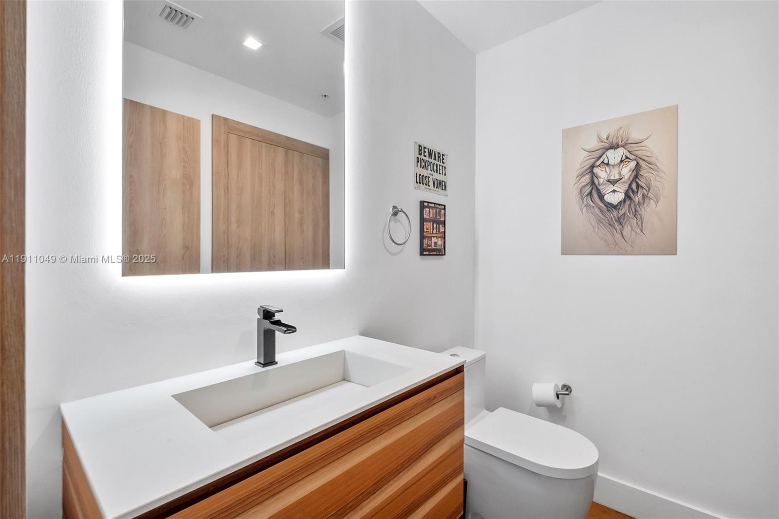 A modern bathroom features a floating wood vanity, a backlit mirror, and a lion wall print — 3470 E Coast Ave, Miami FL 33137, MIAMI, FL