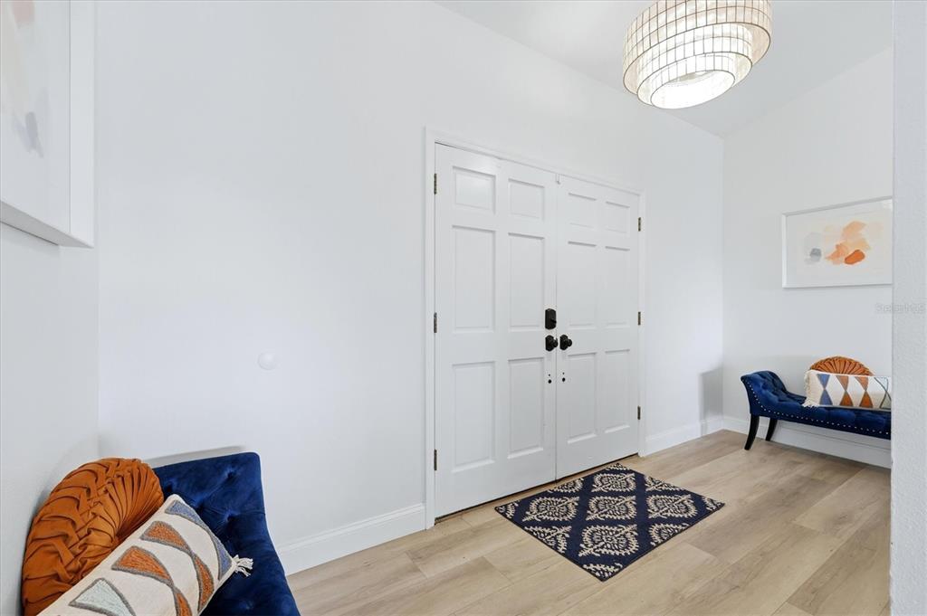 A bright entryway features white double doors, light wood flooring, and two blue velvet benches — 1649 MANOR ROAD, ENGLEWOOD, FL