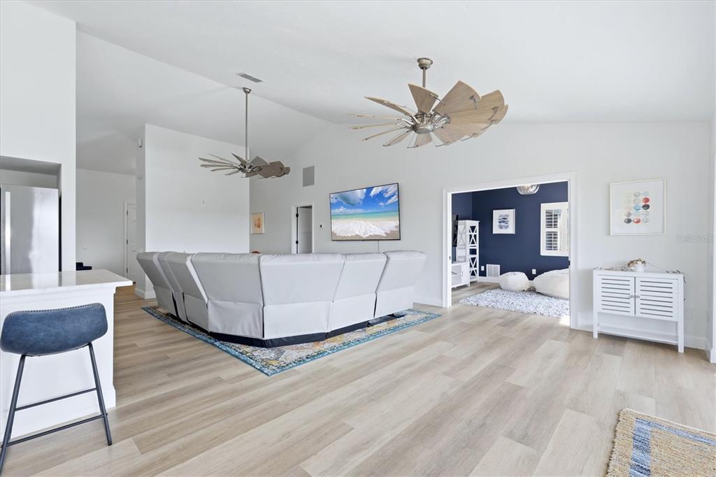 A living room features light wood flooring, a large sectional sofa, and two windmill-style ceiling fans — 1649 MANOR ROAD, ENGLEWOOD, FL