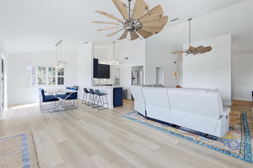 An open-concept living and dining area features light wood flooring, a kitchen island, and ceiling fans — 1649 MANOR ROAD, ENGLEWOOD, FL