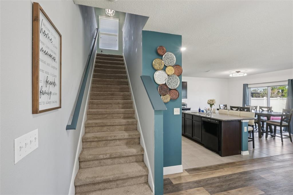 A carpeted staircase leads to an upper floor next to a kitchen with dark cabinetry — 11168 LELAND GROVES DRIVE, RIVERVIEW, FL
