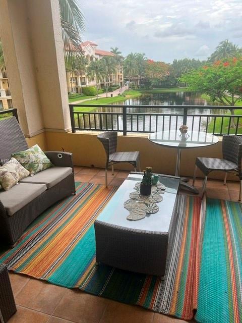 A balcony features wicker furniture, a glass-topped coffee table, and a view of a lake — 16102 Emerald Estates Dr # 235, Weston FL 33331, WESTON, FL